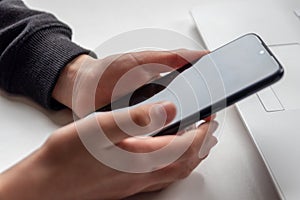 European child hands holding black smartphone with fingers and black screen on white desk infront of white notebook at school