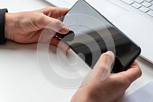 European child hands holding black smartphone with fingers and black screen on white desk infront of white notebook at school