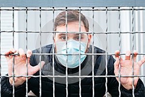 European coronavirus. Portrait of caucasian man wearing facial hygienic mask, respiratory protection mask in cage quarantine, stop