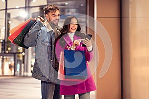 European couple enjoying online shopping on smartphone standing near mall