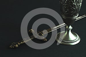 European dagger-stylet replica with bronze handle decorated with medieval original pattern and tin cup for wine on black