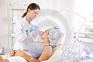 European doctor making Beauty procedure to brunette girl & x28;atomizing pen& x29;