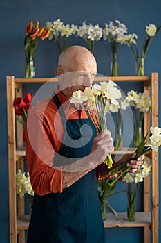 European elderly man florist inhales the smell of flowers.