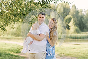 A European family in the park on a summer day. Happy and smiling mom, dad and little son in their arms. Dad plus size