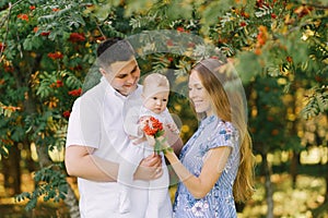 A European family in the park on a summer day. Mom, dad and little son are smiling in their arms