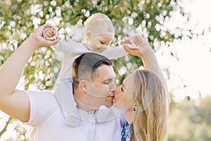 A European family in the park on a summer day. Mom, dad and little son in their arms. Parents kiss each other