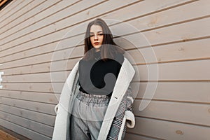 European fashionable young woman model in gray stylish pants in a black shirt in an checkered jacket posing standing