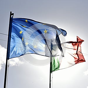 European flag and italian flag waving together in a clear blue sky. Relationship between the European Union and the Italy.