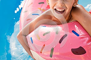A European girl bathes in a blue pool in a pink larger rubber ring. Wet hair and a happy smile. Waves, hotel and beach
