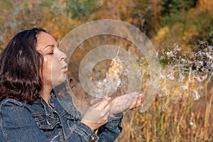 A European girl with black hair blows on a cattail in the hand with which fluff is flying.