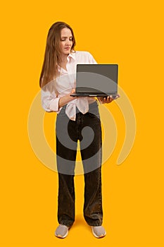 European girl holding laptop computer with blank black screen workspace area. Isolated on yellow background studio portrait. Copy