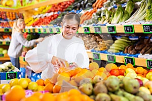 European girl purchaser choosing oranges in a grocery store