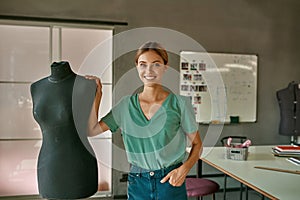 European girl tailor near mannequin look at camera