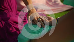 European girls friends in dresses sitting in a circle holding each other`s hands in nature with green grass on the background