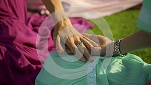 European girls friends in dresses sitting in a circle holding each other`s hands in nature with green grass on the background