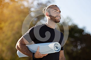 European guy in activewear holds yoga mat on outdoor workout