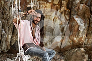 European guy with dreadlocks, asian appearance sitting on a swing on an island, posing