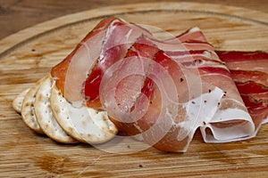 European ham called speck on wooden board with bread slices