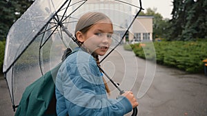 European happy little girl walking city street outside in rain with umbrella back views choolgirl going childhood