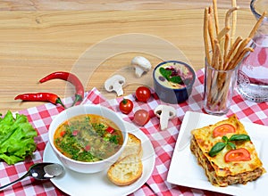 European lunch - vegetables soup, lasagna and dessert served on a wooden table. Italian food background with a copy space/