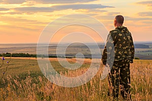 A European male farmer, 40-45 years old, stands in full growth in a field in the summer at dawn in the warm sun against