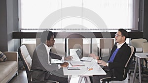 European man and African American man sitting in armchairs and negotiate