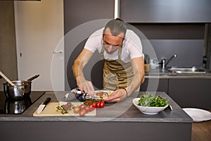 European man in beige chef's apron, standing at kitchen counter and using kitchen towel, removing traces of tomato