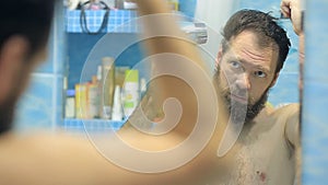 European man blows dry hair and beard in the bathroom in front of the mirror