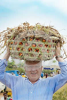 European man carries heavy tomato basket on head like African women do