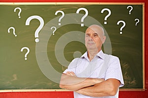European man crossed his arms on the background of a lot of white question marks on a chalkboard for chalk, text, concept close-up