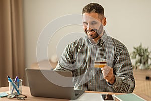European man holding credit card shopping online on laptop indoor