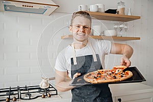 European man holds slice of fresh pizza on bright kitchen background