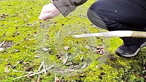 European man whittling a stick with a sharp knife in slow motion as outdoor adventure in a forest in winter hiking tour outdoors