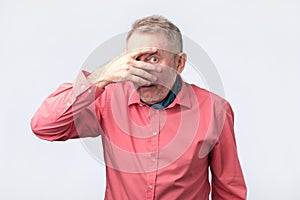 European mature man covering his face by hand and peeping at camera