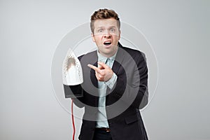 European mature man in suit holding electric iron with dirty burned spot