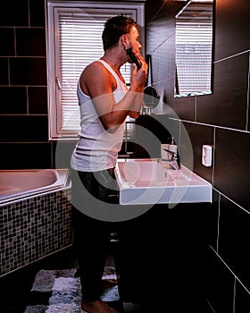 European men in bathroom shaving with electric device,Close up portrait of a handsome shirtless man shaving beard with