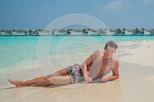 European sexy handsome man enjoying sun bath at tropical sandy beach at island luxury resort