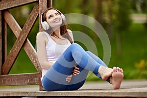 Smiling shoeless woman in cordless headphones listens to music in park.