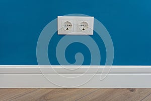 European standard 220 volt wall electrical outlet on wall with baseboard and hardwood floor