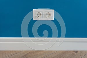 European standard 220 volt wall electrical outlet on wall with baseboard and hardwood floor photo
