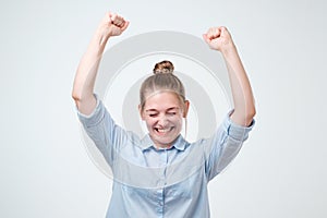 European strong successful young female winner in blue shirt raising arms exclaiming with joy and excitement.