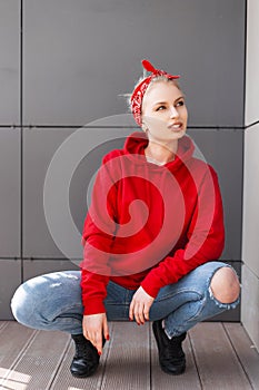 European stylish young blond woman in a fashionable red hooded sweatshirt in a vintage bandana in black boots in a blue jeans