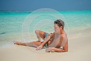 European  tanned handsome sexy man wearing swimming shorts at tropical sandy beach at island luxury resort