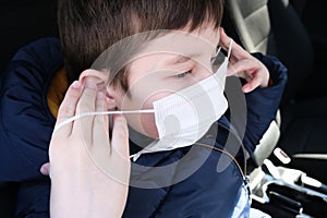 A european teenage boy in car putting on white protective surgical medical face mask as a protection against virus disease,