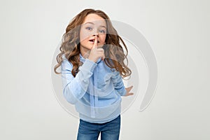 European teenage girl in a blue hoodie asks to be quieter covering her mouth on a white background with copy space