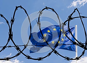 European Union EU flag against a blue sky superimposed with barbed wire relating to potentially a closed off bloc to non-EU