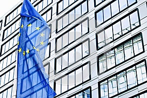 European Union flag waving in front of modern corporate office building, symbol of EU Parliament, Commission and Council