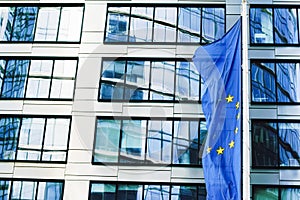 European Union flag waving in front of modern corporate office building, symbol of EU Parliament, Commission and Council