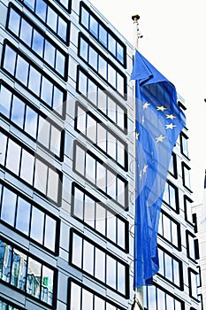 European Union flag waving in front of modern corporate office building, symbol of EU Parliament, Commission and Council
