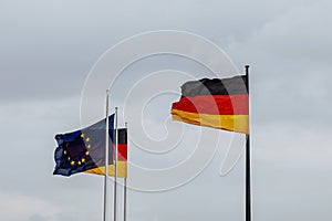 European Union and German flags fluttering against a cloudy sky